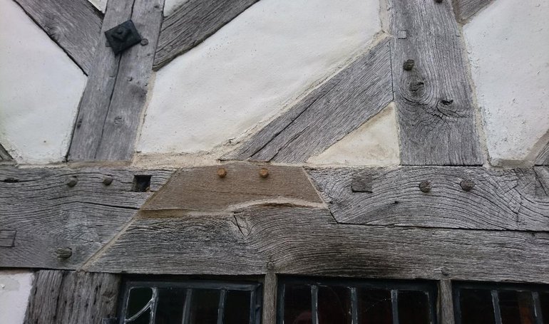 A wooden beam above a window which has been repaired with a new section of timber.