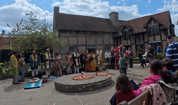 Image showing a group of performers around a small wooden stage in the gardens of Shakespeare's Birthplace with audience members watching