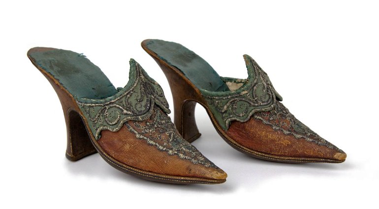 Shoes, c. 1760-1770. A pair of women's shoes, said to have been worn by Mrs Garrick at the Garrick Jubilee of 1769. They are made from red leather and trimmed and partly lined with blue/green silk, and decorated with metal thread. Shoes are backless, with